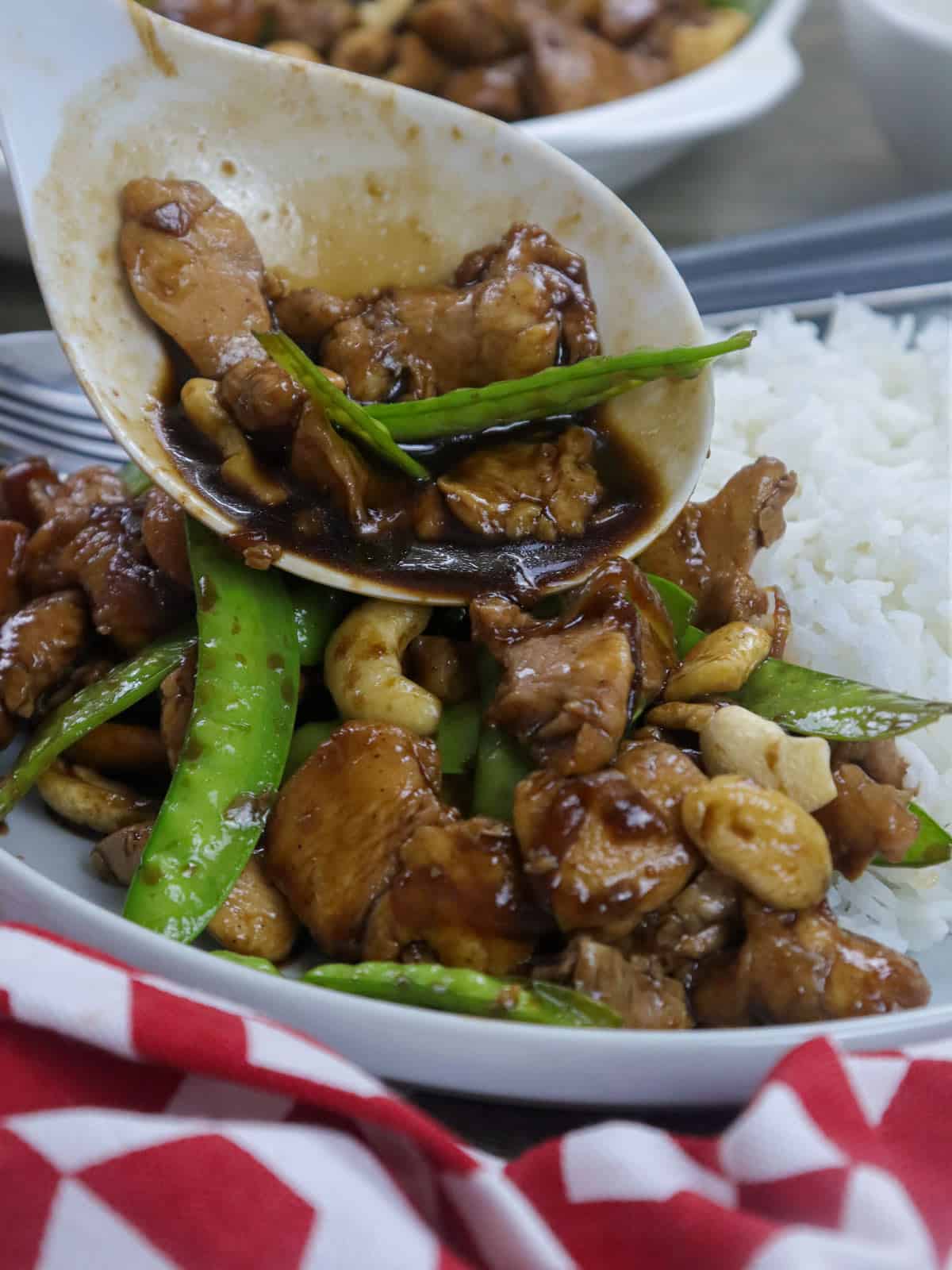 serving Cashew Chicken in a white bowl with a plate of steamed rice in the background.