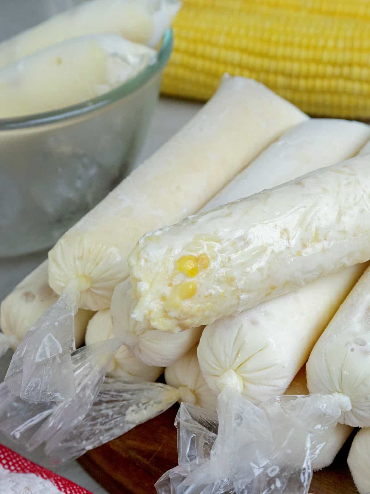 frozen mais con queso ice pops on a wooden plate with corn on the cob in the background.