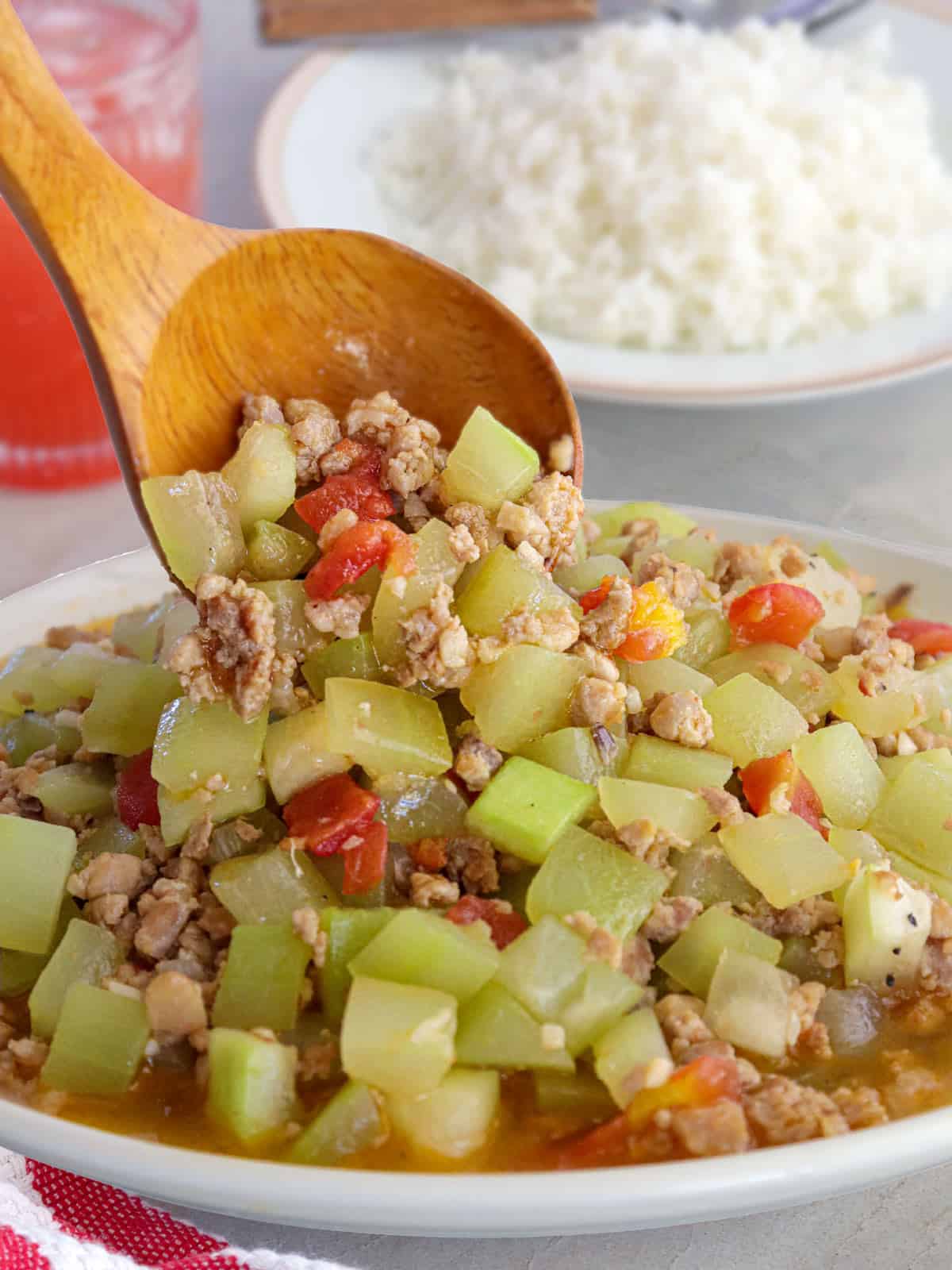 serving Ilocano-style ginisang upo with ground pork in a white bowl using a wooden spoon.