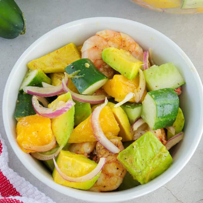 mango avocado cucumber salad with grilled shrimp in a white bowl.