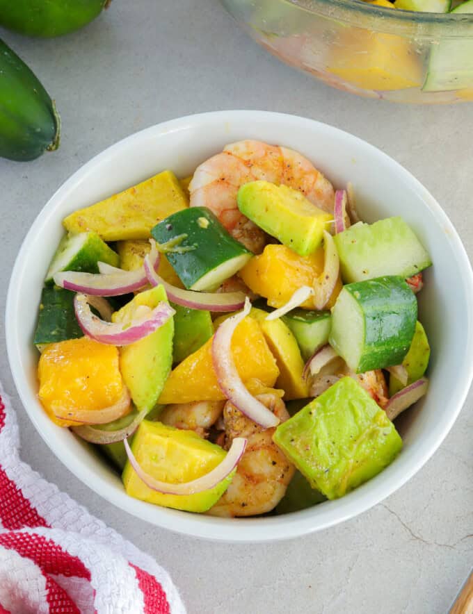 mango avocado cucumber salad with grilled shrimp in a white bowl.