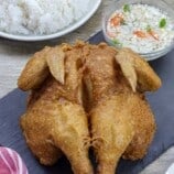 crispy fried butterflied chicken on serving board with steamed rice in the background.