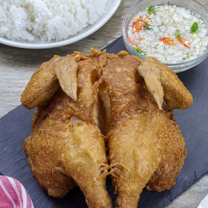 crispy fried butterflied chicken on serving board with steamed rice in the background.