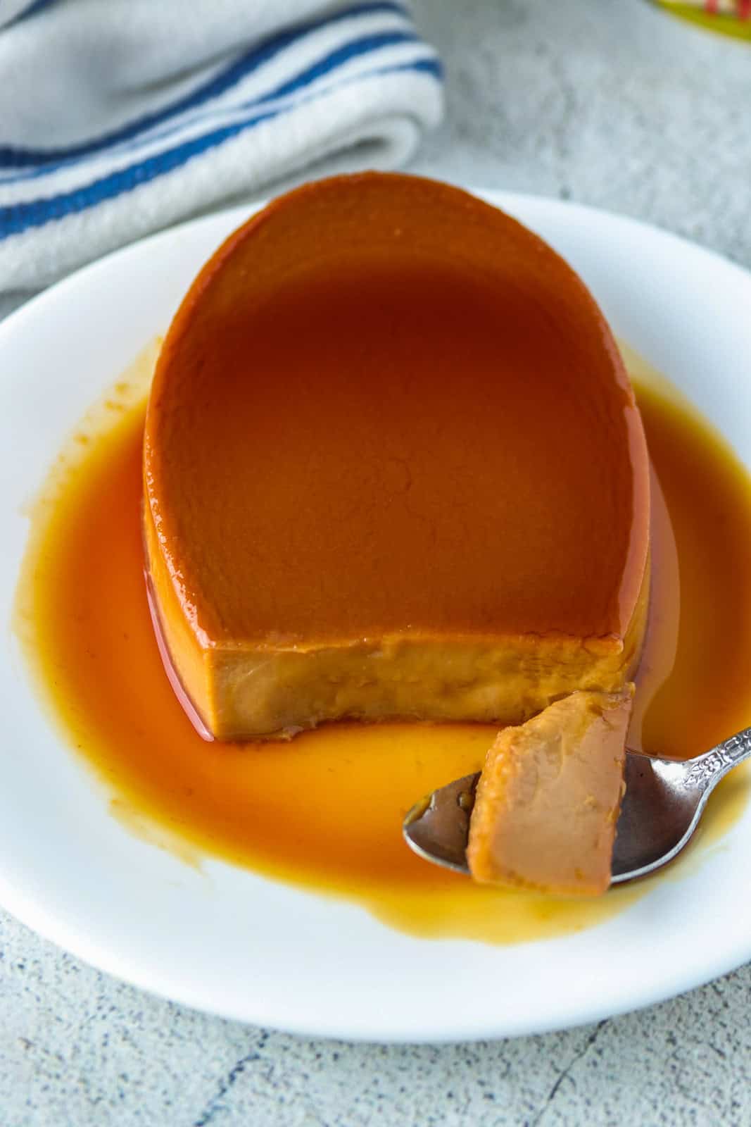 eating a slice of caramel flan with a spoon on a white plate.