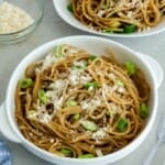 Asian Garlic Noodles in a white bowls with a little bowl of parmesan cheese in the background.