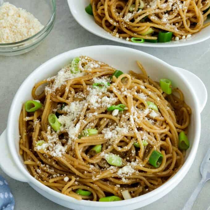 Asian Garlic Noodles in a white bowls with a little bowl of parmesan cheese in the background.