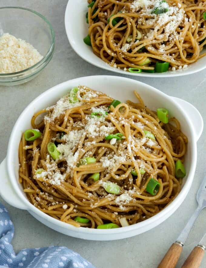 Asian Garlic Noodles in a white bowls with a little bowl of parmesan cheese in the background.