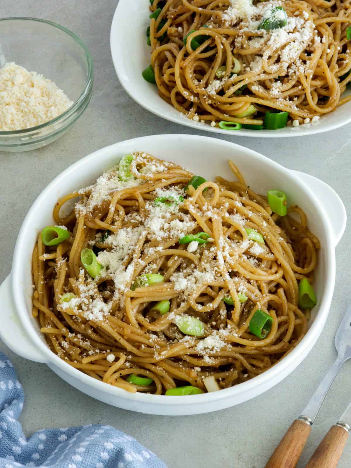 Asian Garlic Noodles in a white bowls with a little bowl of parmesan cheese in the background.