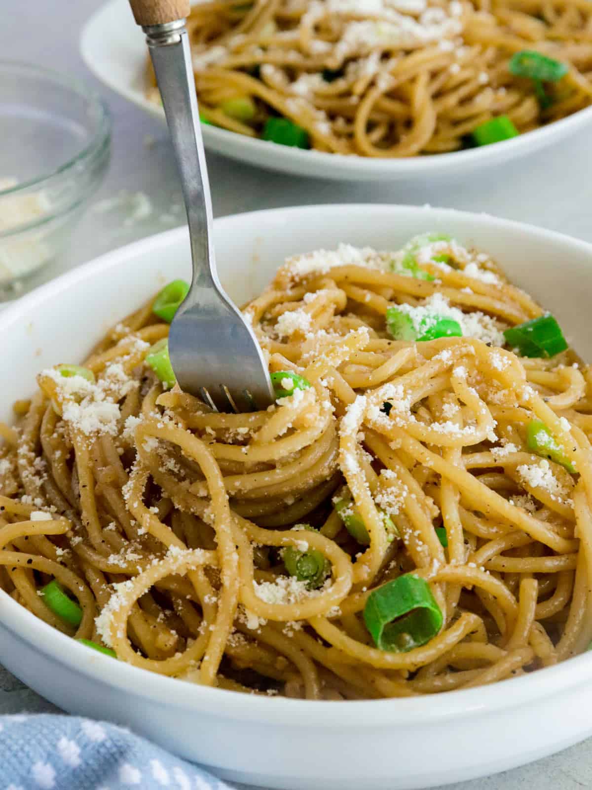 eating Asian Garlic Noodles in a white bowl with a fork.