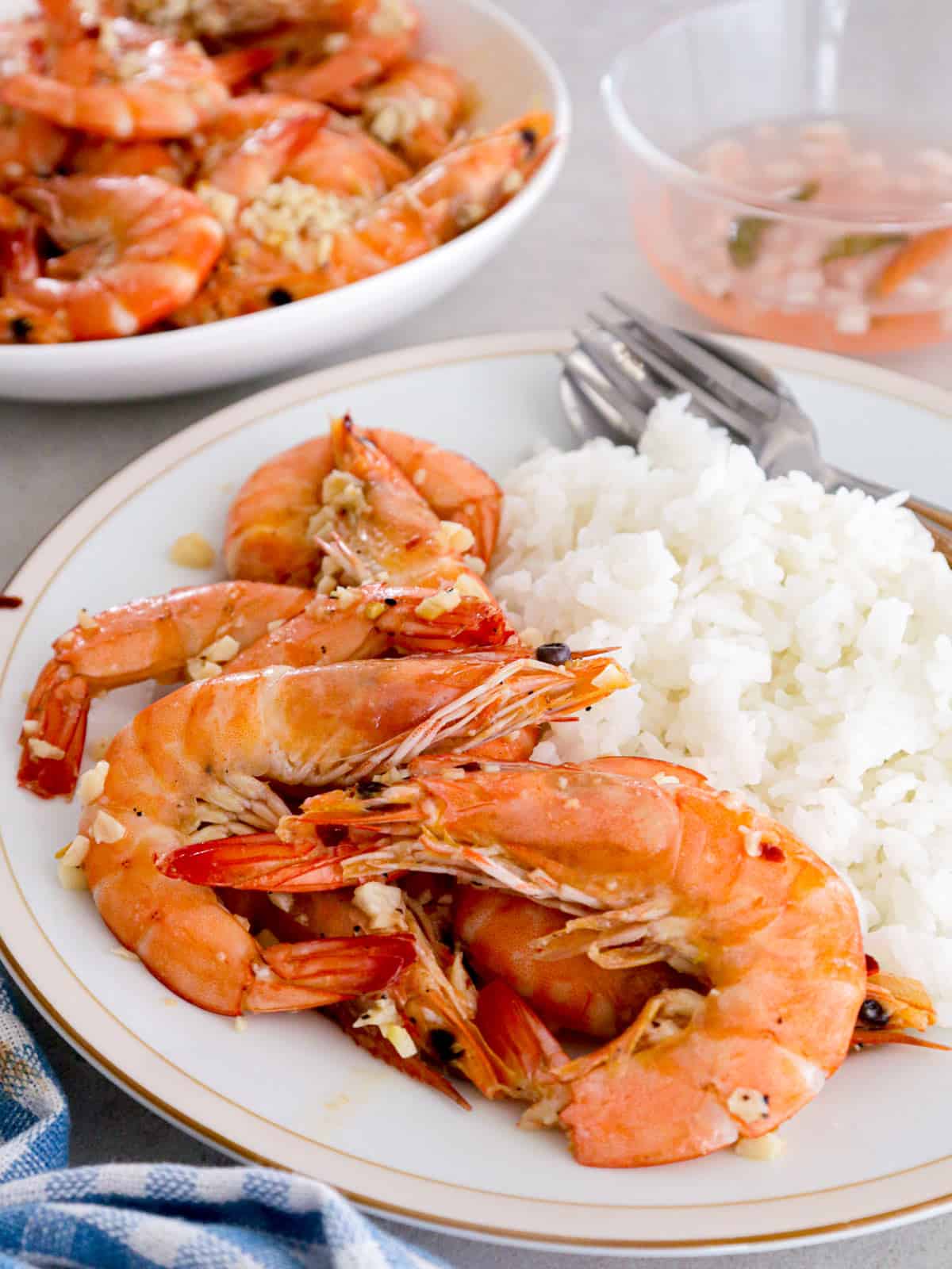 Filipino garlic butter shrimp and steamed rice on a plate and vinegar dipping sauce in a bowl in the background.