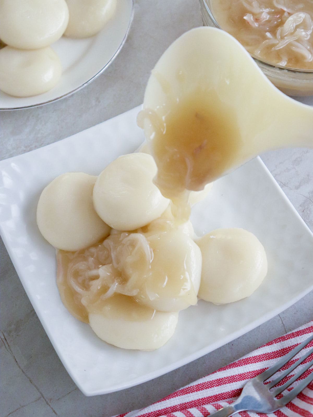 pouring bukayo syrup over palitaw patties on a white plate.